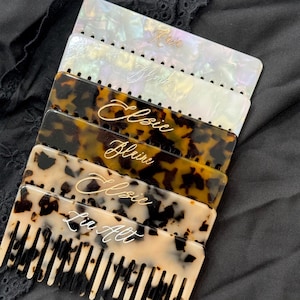 May include: A stack of five tortoiseshell combs with different names engraved on them. The names are "Rain", "Blaine", "Elsie", "Blaine", and "La  Aft".