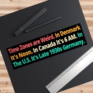 May include: A black rectangular sticker with the text "Time Zones are Weird. In Denmark It's Noon. In Canada It's 6 AM. In The U.S. It's Late 1930s Germany." in various colors. A black pen and a ruler are also visible.