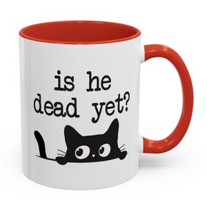 May include: White ceramic coffee mug with a red rim and handle. The mug has a black cat peeking over the top and the text "is he dead yet?" printed on the front.