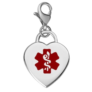 Puede incluir: Un dije de alerta médica plateado en forma de corazón. El dije presenta un símbolo médico rojo sobre un fondo blanco. Incluye un cierre de mosquetón para sujetarlo a una pulsera o collar.