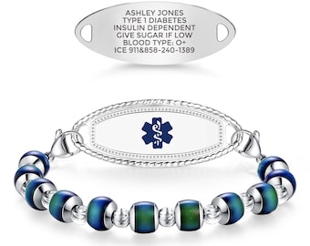 May include: A medical alert bracelet featuring a silver-toned oval plaque with a blue Star of Life emblem, connected to a strand of alternating silver-toned beads and dark blue mood beads. A separate silver oval tag displays the text ASHLEY JONES TYPE 1 DIABETES INSULIN DEPENDENT GIVE SUGAR IF LOW BLOOD TYPE: O+ ICE 911&858-240-1389.
