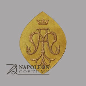 May include: A pointed oval-shaped gold fabric patch featuring intricate gold-tone embroidery of a stylized monogram with the letters A and M topped by a small crown. The text NAPOLEON COSTUME is printed in the lower left corner of the image.
