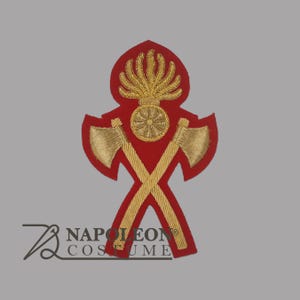 May include: A red and gold embroidered patch with crossed axes, a central wheel design, and a flame-like element at the top. The patch is likely for a costume or uniform, with a decorative design.