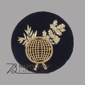 May include: A round, navy blue embroidered patch featuring a gold-colored globe design with a grid pattern. Gold-colored leaves and branches are embroidered around the globe. The patch has the text "NAPOLEON COSTUME" in white.