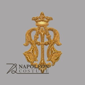 May include: A gold-colored embroidered patch featuring an ornate, symmetrical design with a central vertical pillar topped by a crown, flanked by curved, leaf-like flourishes. The text NAPOLEON COSTUME is printed in black below the design.