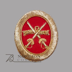 以下が含まれることがあります： 赤色の中心部を持つ、楕円形の金色の刺繍パッチ。中央には、2本の交差した剣と金のリースデザインがあります。このパッチは、おそらく軍事または儀式用のエンブレムです。