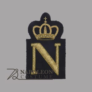 Könnte beinhalten: Ein schwarzer Aufnäher mit einer goldgestickten Krone und dem Buchstaben "N". Der Buchstabe ist ebenfalls goldgestickt. Der Aufnäher hat eine rechteckige Form mit einer Krone oben. Der Text "NAPOLEON COSTUME" befindet sich unten links.