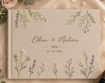 May include: A rectangular beige fabric photo album featuring embroidered wildflowers and the text Ethan & Madison 05-24-2026. The cover is decorated with delicate floral stems in shades of green, white, yellow, and purple, centered on the front.