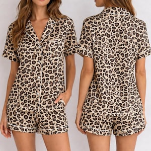 May include: A two-piece pajama set featuring a leopard print pattern. The set includes a short-sleeved button-down shirt and matching shorts, both trimmed with white piping. The fabric has a tan background with dark brown spots.