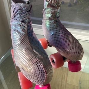 Könnte beinhalten: Ein Paar Rollschuhe mit schillernden Oberteilen und rosa Rollen. Die Rollschuhe haben ein Muster aus kleinen, dunklen Formen auf den Oberteilen. Die Zehenstopper sind leuchtend rosa und die Rollen sind heller rosa.