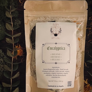 May include: A tan resealable pouch containing bath salts labeled Bain Ritual Eucalyptica. The label lists ingredients including Epsom, Dead Sea, Himalayan, and Celtic salts, eucalyptus, rosemary, calendula, and tea tree oils. Net weight 12 oz.