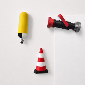 May include: A set of three objects including a yellow and white cylindrical tank with a small nozzle, a black and red fire hose nozzle with a handle, and a red and white traffic cone with a black square base, all arranged on a white surface.