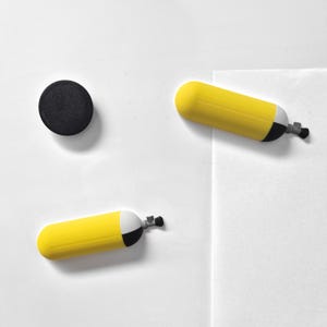 Könnte beinhalten: Ein Set aus drei ausgefallenen Magneten. Zwei gelb-weiße Tauchflaschenmagnete und ein schwarzer runder Magnet sind auf weißem Hintergrund angeordnet. Die Tauchflaschen haben schwarze und silberne Details.