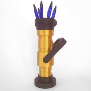 May include: A gold-colored metal fire hose nozzle with a black handle and a black base. The nozzle has a black cap on top with blue pencils sticking out of it.