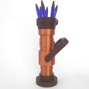 Peut inclure: Une buse de tuyau d'incendie de couleur cuivre avec une poignée noire et une base noire. La buse a un dessus en plastique noir qui contient plusieurs stylos bleus.