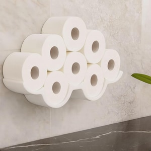 Könnte beinhalten: Ein weißer, wolkenförmiger Toilettenpapierhalter an der Wand, der mehrere Rollen weißes Toilettenpapier hält. Der Halter hat ein glattes, geschwungenes Design und besteht aus einem festen, undurchsichtigen Material. Der Hintergrund ist eine hellfarbige, strukturierte Wand.