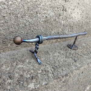 Puede incluir: Manija de puerta de metal forjada a mano con un diseño texturizado en forma de rama. El mango tiene un extremo esférico y un soporte retorcido decorativo. El metal tiene un acabado oscuro e iridiscente con toques de azul y morado.