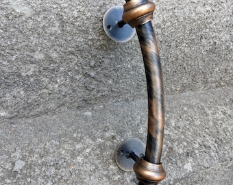 May include: A decorative door handle with a bronze and black finish. The handle has a curved design with a textured appearance and is mounted on a gray stone surface. The handle is approximately 10 inches long.