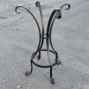 May include: Black wrought iron table base with a decorative design. The base features curved legs and a circular footrest. The top has four mounting plates for attaching a tabletop. The overall design is elegant and suitable for various table sizes.