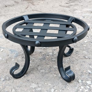 May include: Black metal plant stand with a circular top and a lattice design. The stand has three curved legs with decorative scrollwork at the base. The stand is approximately 12 inches in diameter and 10 inches tall.
