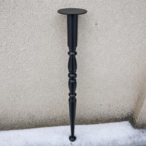 Könnte beinhalten: Ein schwarzes Tischbein mit dekorativem, gedrehtem Design. Das Bein hat eine runde obere Platte und eine sich verjüngende Unterseite. Das Metallbein ist schwarz lackiert. Ungefähr 70 cm hoch.