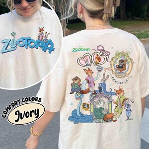 Puede incluir: Camiseta de color marfil con la palabra "Zootopia" en azul y personajes de dibujos animados. La parte trasera de la camiseta muestra un gr&aacute;fico m&aacute;s grande con varios personajes de Zootopia y el logotipo de Disney. La camiseta es de color confort.