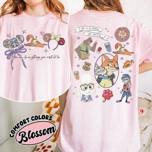 Puede incluir: Camiseta rosa claro con personajes de dibujos animados y la frase "You can be anything you wish to be." El dise&ntilde;o incluye un zorro, un conejo, un perezoso y otros personajes. La camiseta est&aacute; etiquetada como "Comfort Colors Blossom."