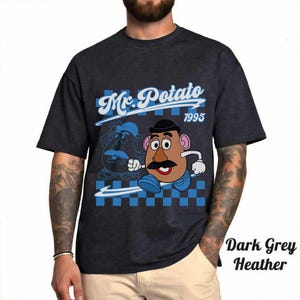 May include: Dark grey heather t-shirt featuring a Mr. Potato Head graphic. The design includes the text "Mr. Potato 1995" in a blue and white checkered background. The shirt has short sleeves.