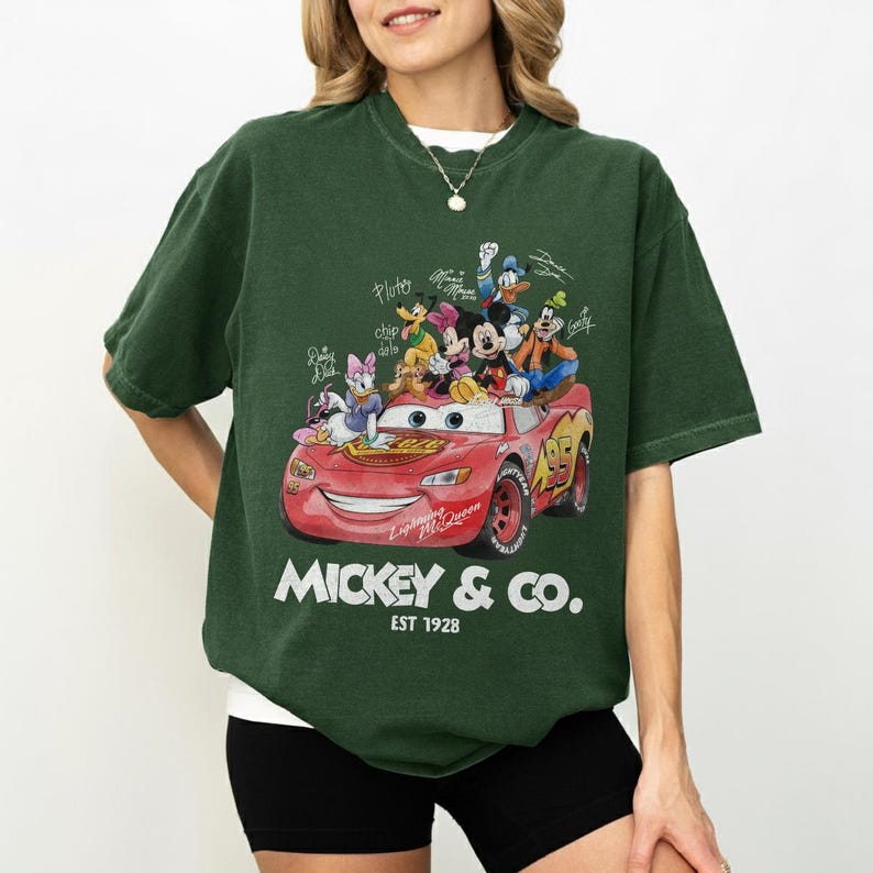 May include: Dark green t-shirt featuring a red cartoon car with Mickey Mouse and friends. The car has the number 95 on it and the text "Mickey & Co. Est 1928". The shirt is a crew neck.