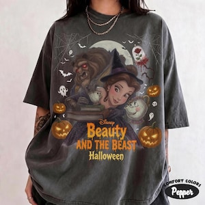 Può includere: Una t-shirt grigio antracite a maniche corte con una grafica di Halloween raffigurante Belle e la Bestia. Il design include zucche, fantasmi, pipistrelli, una rosa sotto una campana di vetro e il testo Disney Beauty and the Beast Halloween.