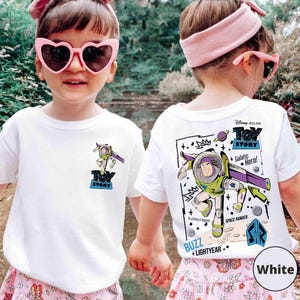 K&ouml;nnte beinhalten: Wei&szlig;e T-Shirts mit einem Buzz Lightyear-Motiv aus Toy Story. Die Vorderseite hat ein kleines Design, die R&uuml;ckseite ein gr&ouml;&szlig;eres mit "Galactic Hero!" und "Space Ranger". Das Disney Pixar-Logo ist ebenfalls sichtbar.