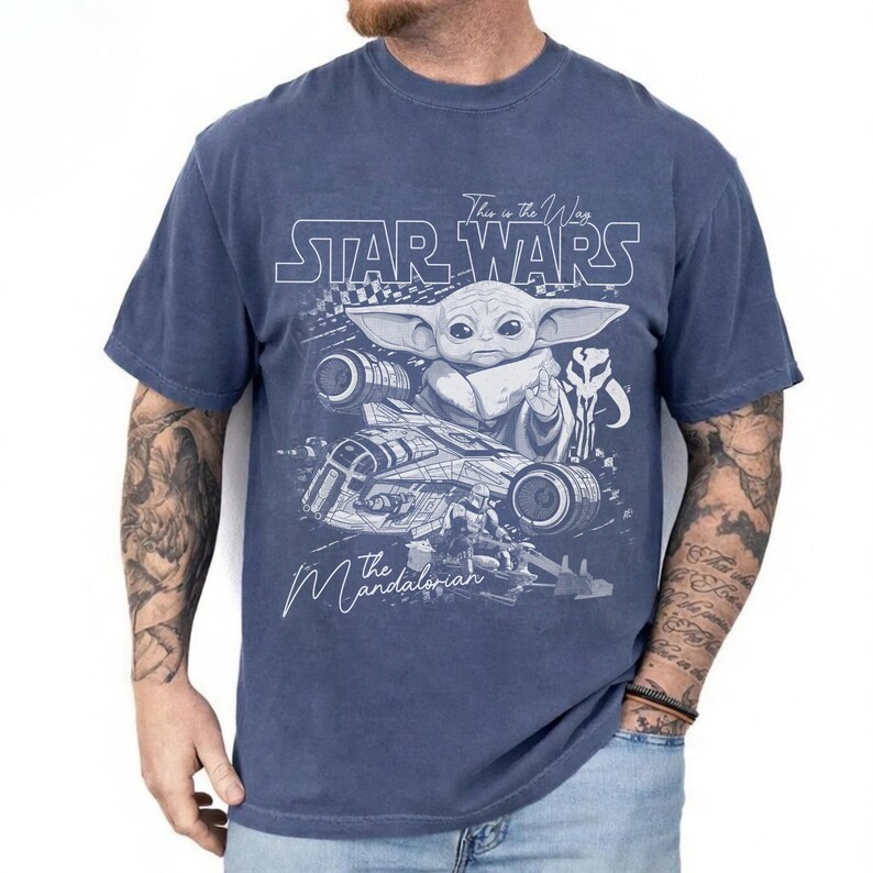 Puede incluir: Una camiseta azul de manga corta con un estampado gr&aacute;fico blanco de Grogu, una nave espacial y el texto Star Wars, This is the Way y The Mandalorian. El dise&ntilde;o incluye un patr&oacute;n de cuadros y un icono de calavera sobre una tela azul deste&ntilde;ida.
