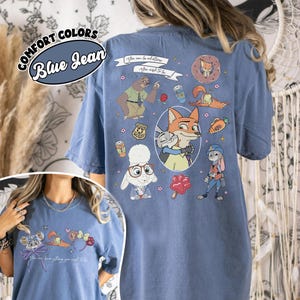 Puede incluir: Camiseta azul vaquero con personajes de dibujos animados y el texto "You can be anything you wish to be." La camiseta presenta varios personajes e iconos. Las palabras "Comfort Colors" est&aacute;n encima de las palabras "Blue Jean".