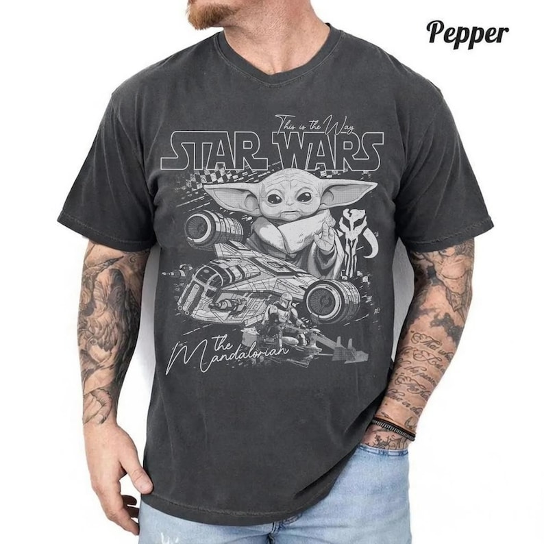 Puede incluir: Una camiseta de manga corta en color gris carb&oacute;n con un estampado gr&aacute;fico de Grogu y una nave espacial de Star Wars: The Mandalorian. El dise&ntilde;o incluye el texto Star Wars y The Mandalorian en blanco, con una est&eacute;tica desgastada y vintage.