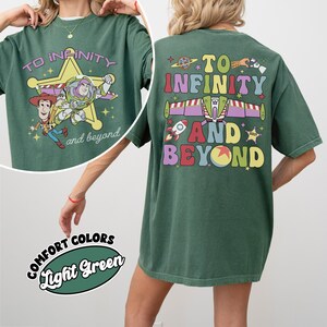 May include: A light green t-shirt featuring the phrase "TO INFINITY and beyond" with cartoon characters and a star design. The back of the shirt has the same phrase with a rocket ship and planet design. The shirt is labeled "Comfort Colors Light Green".