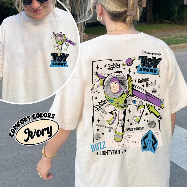 K&ouml;nnte beinhalten: Elfenbeinfarbenes Langarm-T-Shirt mit Buzz Lightyear aus Toy Story. Die Vorderseite hat eine kleine Grafik, w&auml;hrend die R&uuml;ckseite ein gr&ouml;&szlig;eres Design mit dem Text "Toy Story", "Galactic Hero" und "Buzz + Lightyear" zeigt. Das Shirt ist Teil der "Comfort Colors"-Kollektion.