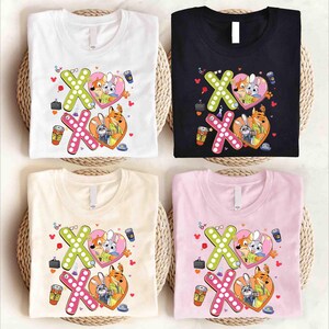 May include: Four t-shirts in white, black, beige, and pink, each featuring a graphic design with the characters from Zootopia. The design includes the letters "XO" with a heart, and other small illustrations.