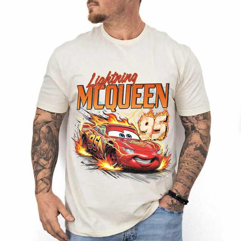 Puede incluir: Camiseta color crema con un gr&aacute;fico de Rayo McQueen, un coche de carreras rojo con el n&uacute;mero 95, y el texto "Lightning McQueen" en naranja y rojo. El dise&ntilde;o incluye llamas y l&iacute;neas de velocidad.