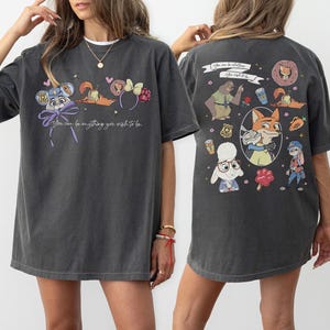 Puede incluir: Camiseta gris oscuro con personajes de dibujos animados y el texto "You can be anything you wish to be." La parte trasera de la camiseta tiene m&aacute;s personajes de dibujos animados y el texto "After all, to be."