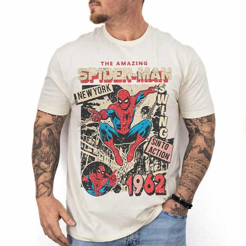 Pode incluir: Camiseta creme com um gr&aacute;fico vintage do Homem-Aranha. O design inclui as palavras "The Amazing Spider-Man", "New York" e "1962". O Homem-Aranha &eacute; retratado em seu cl&aacute;ssico traje vermelho e azul.