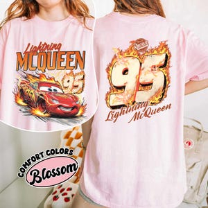 May include: Light pink t-shirt featuring Lightning McQueen from the Cars movie. The front graphic shows McQueen racing with flames, the number 95, and the text "Lightning McQueen". The back has a large "95" with flames and "Lightning McQueen" text.