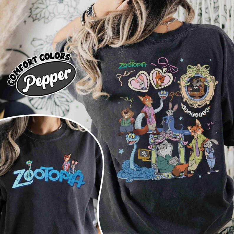 Puede incluir: Camiseta gris oscuro con la palabra "Zootopia" en azul y un gr&aacute;fico de personajes de la pel&iacute;cula de Disney. La parte trasera de la camiseta muestra un dise&ntilde;o m&aacute;s grande con varios personajes y el t&iacute;tulo de la pel&iacute;cula.