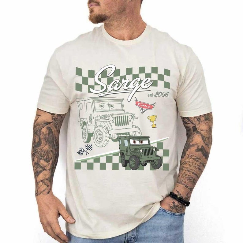 May include: Cream-coloured t-shirt with a graphic of the character Sarge from the film Cars. The design includes a green and white chequered pattern, the name "Sarge", and the text "est. 2006". A cartoon jeep is also featured.