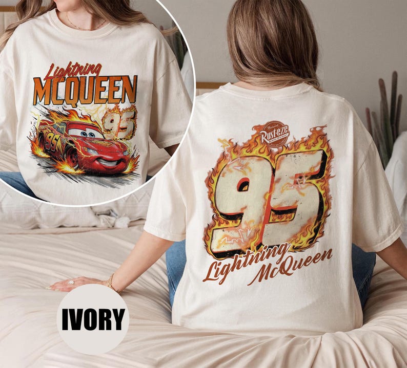May include: Ivory-colored t-shirt featuring a graphic of Lightning McQueen from the Cars movie. The front design shows the car with flames and the text "Lightning McQueen 95." The back displays "95" in flames and the text "Lightning McQueen."