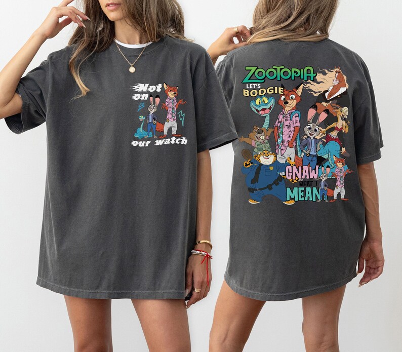 May include: Dark grey t-shirt featuring a colorful graphic from the movie Zootopia. The front of the shirt has the text "Not on our watch" with cartoon characters. The back of the shirt has the text "Zootopia" and "Let's Boogie".
