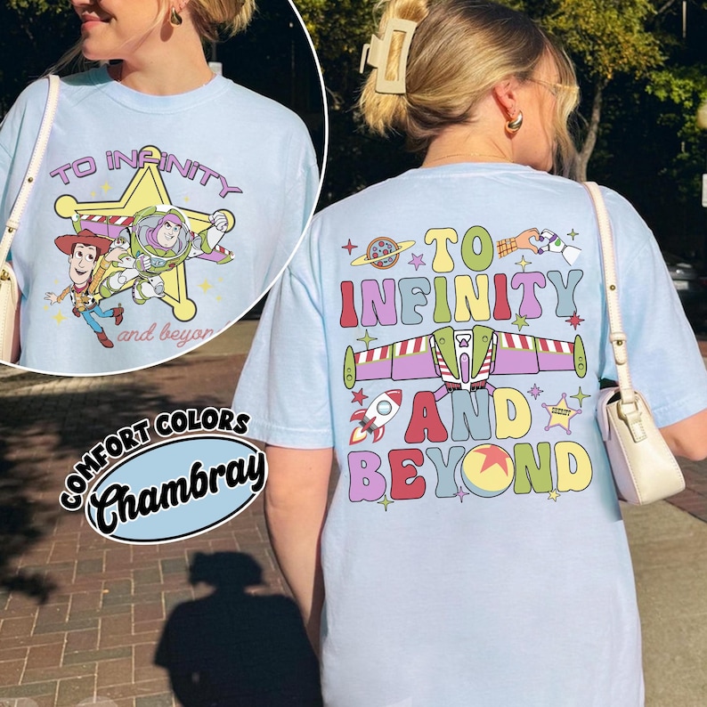 May include: Light blue t-shirt with a graphic featuring Woody, Buzz Lightyear, and the text "To Infinity and Beyond." The back of the shirt repeats the phrase with a rocket and space-themed design. The shirt is labeled "Comfort Colors Chambray."