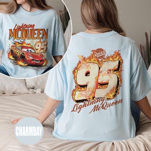May include: Light blue t-shirt featuring Lightning McQueen from the Cars movie. The front graphic shows the character in flames with the text "Lightning McQueen 95". The back displays a large "95" in flames with "Lightning McQueen" below.