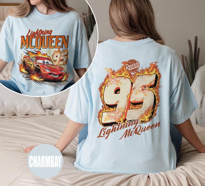 May include: Light blue t-shirt featuring Lightning McQueen from the Cars movie. The front graphic shows the character in flames with the text "Lightning McQueen 95". The back displays a large "95" in flames with "Lightning McQueen" below.