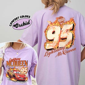 May include: A light purple t-shirt with the text "Lightning McQueen" and the number "95" in a fiery design. The shirt also features the words "Comfort Colors" and "Orchid".