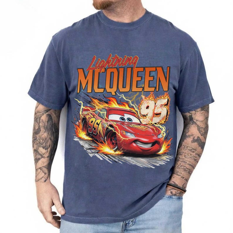 Puede incluir: Camiseta azul con Lightning McQueen de la pel&iacute;cula Cars. El dise&ntilde;o incluye el texto "Lightning McQueen" en naranja, el n&uacute;mero "95" y un coche de carreras rojo con llamas.